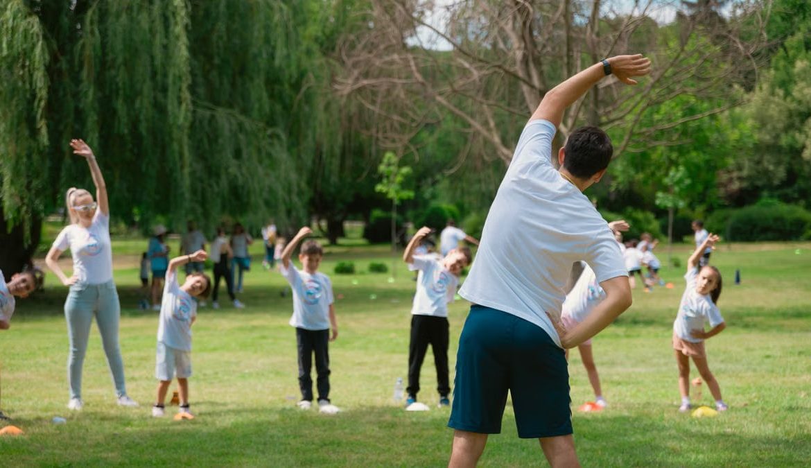 Children and instructors stretching in a park during a summer physical education class.