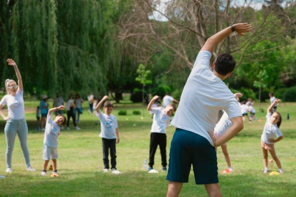 Children and instructors stretching in a park during a summer physical education class.