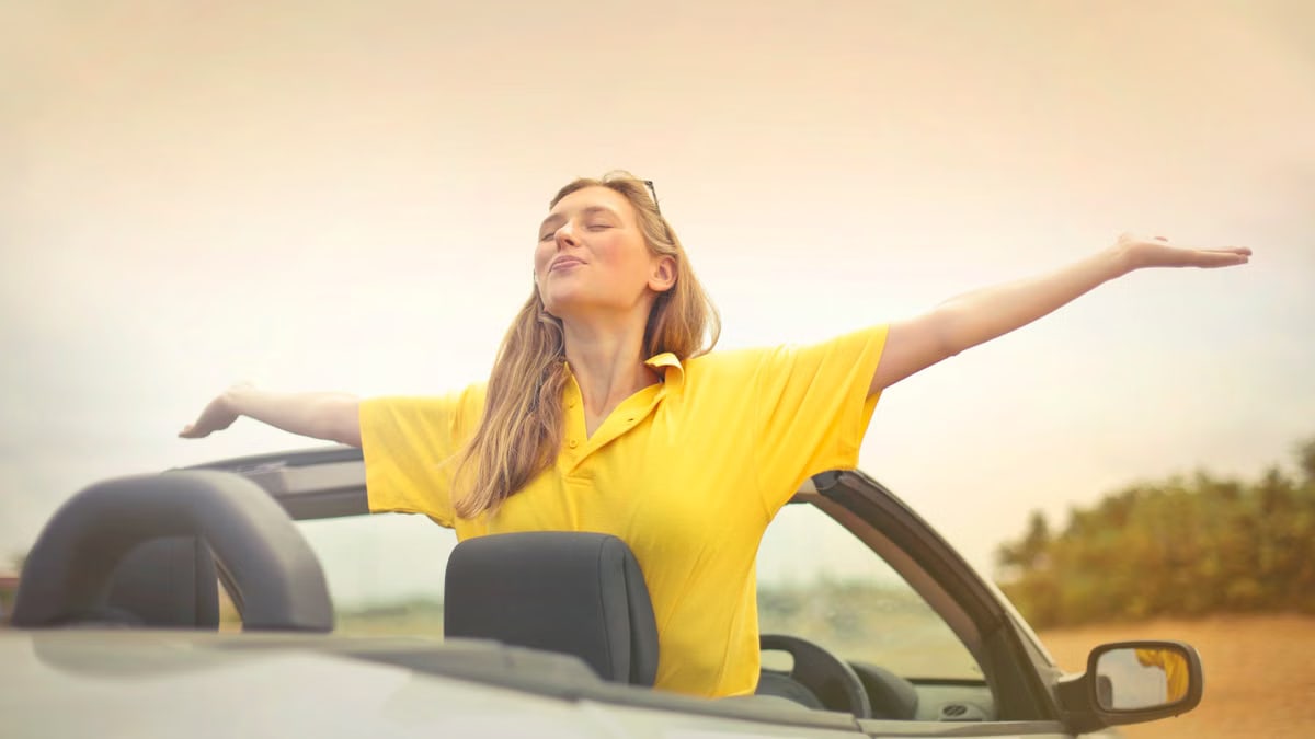 A cheerful woman in a yellow shirt enjoys freedom on a sunny drive in a convertible.